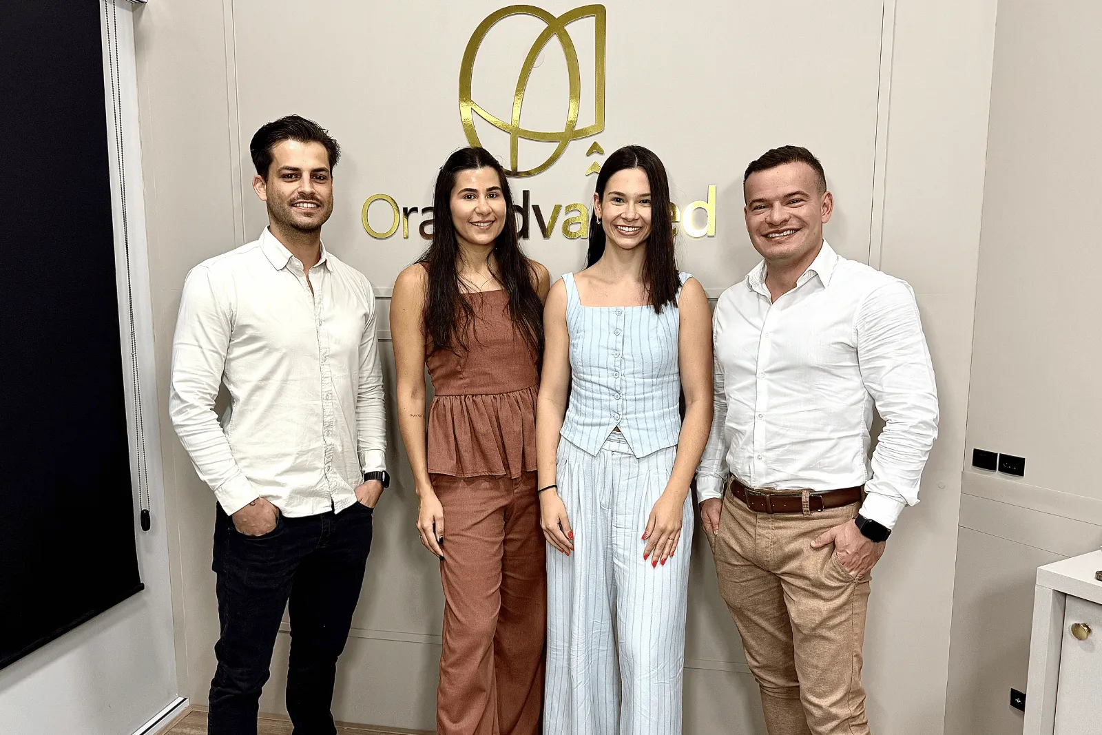 Quatro pessoas da equipe da Oral Advanced em pé, diante do logo dourado da clínica
