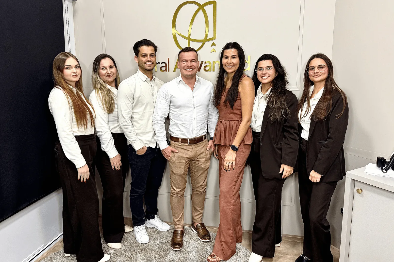 Sete pessoas da equipe da Oral Advanced lado a lado na clínica, com o logo dourado ao fundo