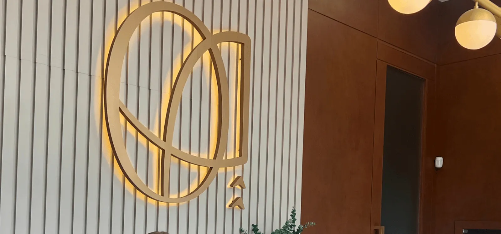 Plano detalhe do logo da Oral Advanced, iluminado por trás, na parede de ripas da recepção