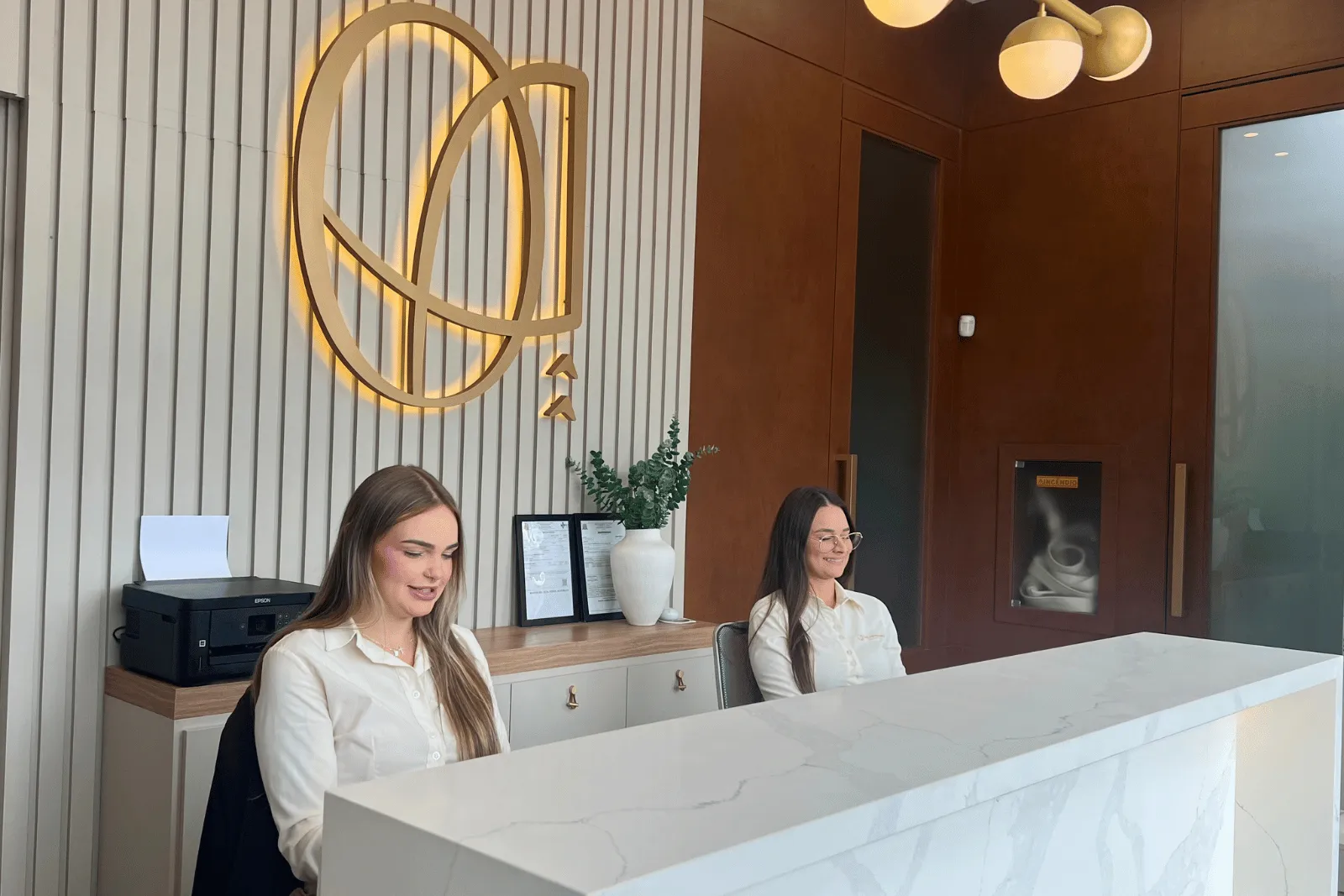 Recepção da Oral Advanced: balcão de mármore, duas recepcionistas e o logo iluminado na parede de ripas
